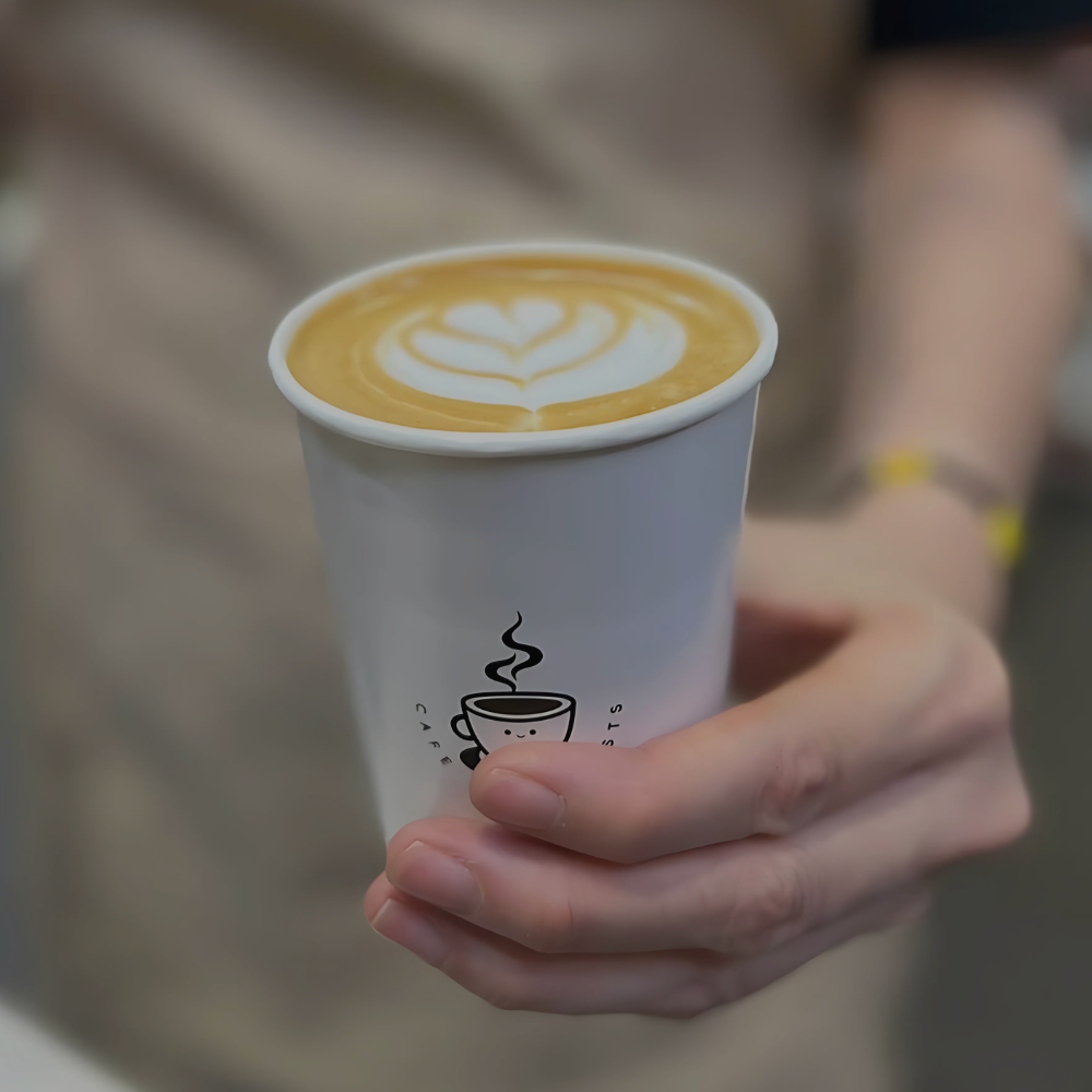 Hand holding a paper cup with a cappuccino and latte art design.